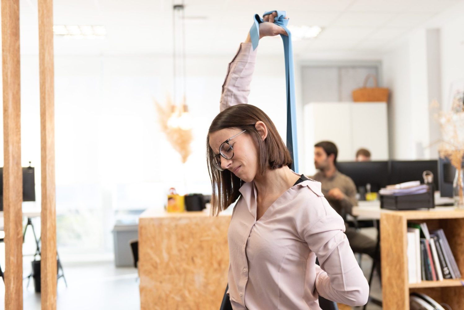 woman-with-backache-back-pain-stretching-with-pilates-rubber-band-office-min